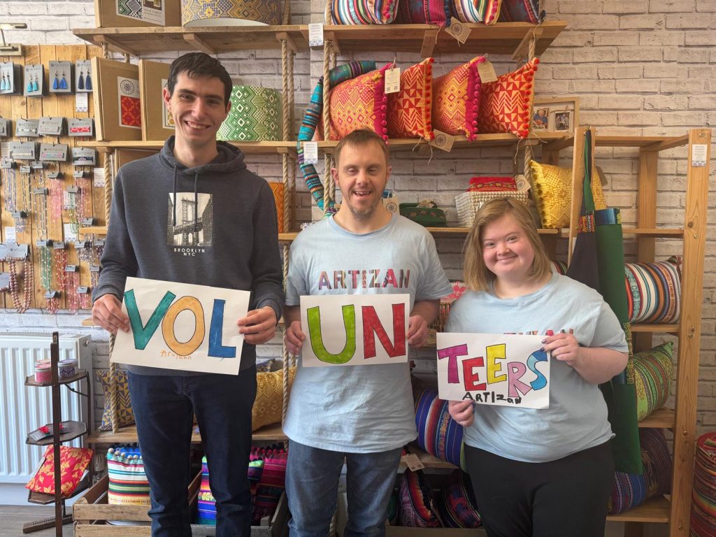 Three volunteers in our Harrogate shop holding up handmade signs that say volunteers